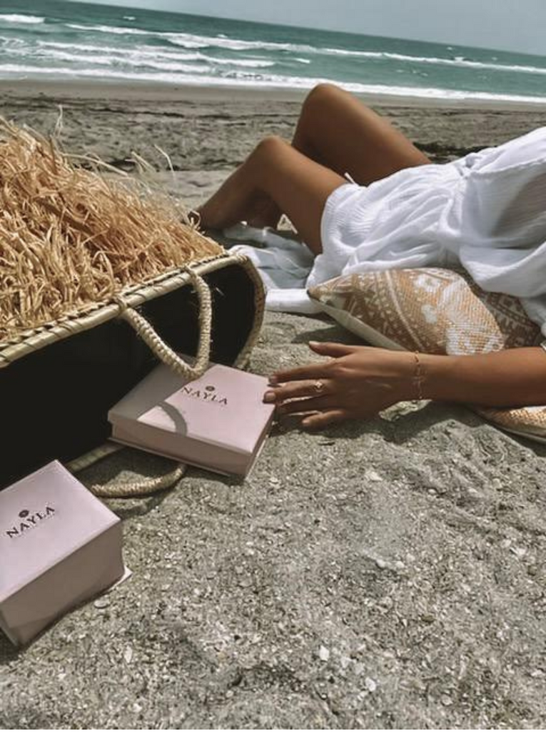 Person sitting on a beach with a bag and a box labeled 'NATIA'.